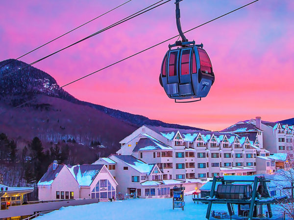 Gondola in motion up to the mountain in the distance with the resort in Lincoln, NH below with a beautiful sunset behind