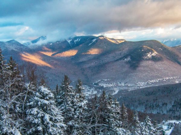 View into the snowy mountains in Lincoln, NH with snow covering the mountains and trees and clouds on top of the mountains