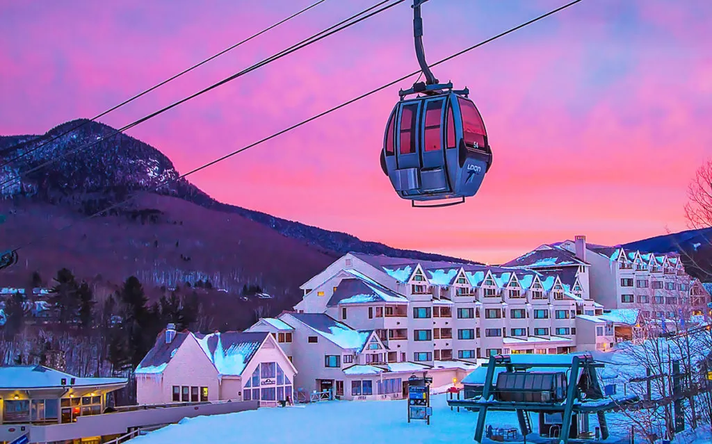 Gondola in motion up to the mountain in the distance with the resort in Lincoln, NH below with a beautiful sunset behind