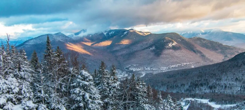 View into the snowy mountains in Lincoln, NH with snow covering the mountains and trees and clouds on top of the mountains