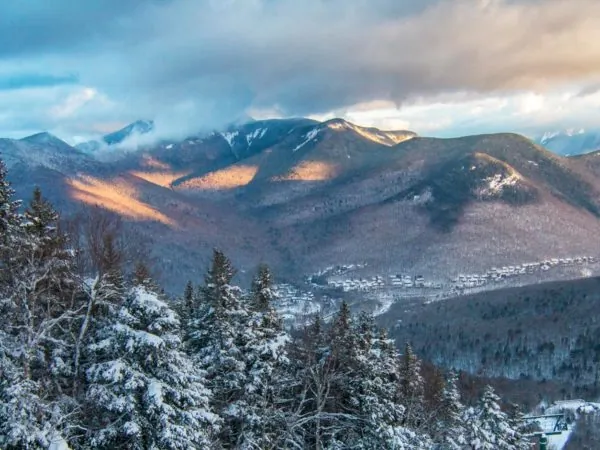View into the snowy mountains in Lincoln, NH with snow covering the mountains and trees and clouds on top of the mountains
